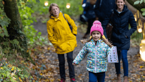 Young girl running through the woods in autumn wearing warm clothing and holding a trail sheet